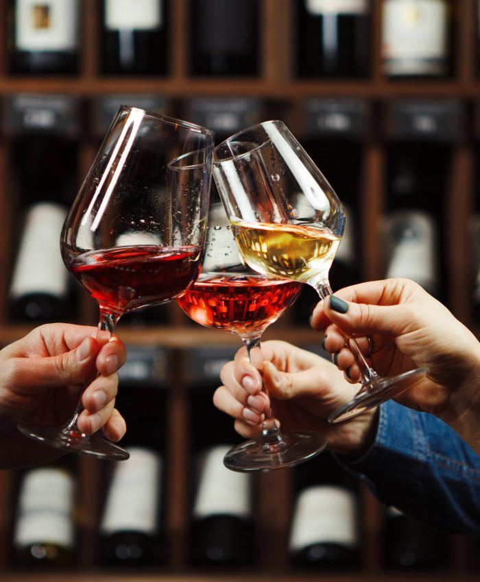 People in good mood clink glasses, celebrating together, photo focus on hands woman and man tasting degustation different types of wine, alcohol beverage to relax, bottles on shelves on background